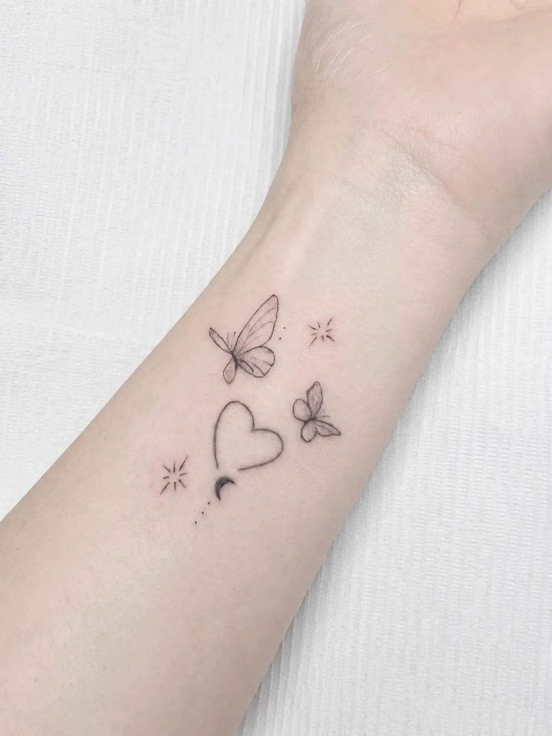 Composición fine line con dos mariposas pequeñas, un corazón y cuatro estrellas en el tobillo