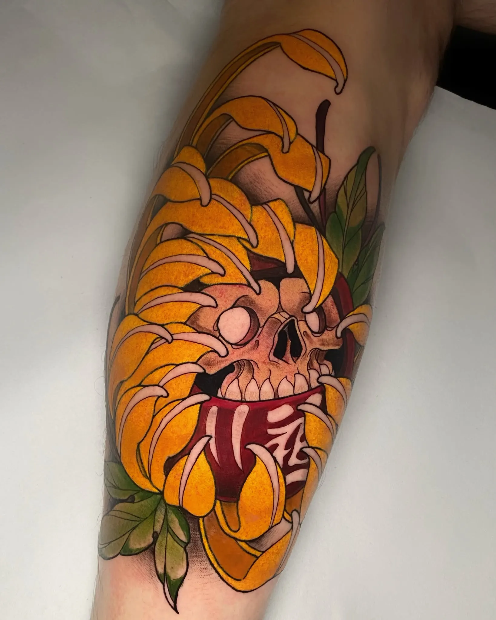 Tatuaje Illustrative Color de un Maneki Neko estilizado con melena de león dorada, garras y hojas verdes, tatuado en la pantorrilla