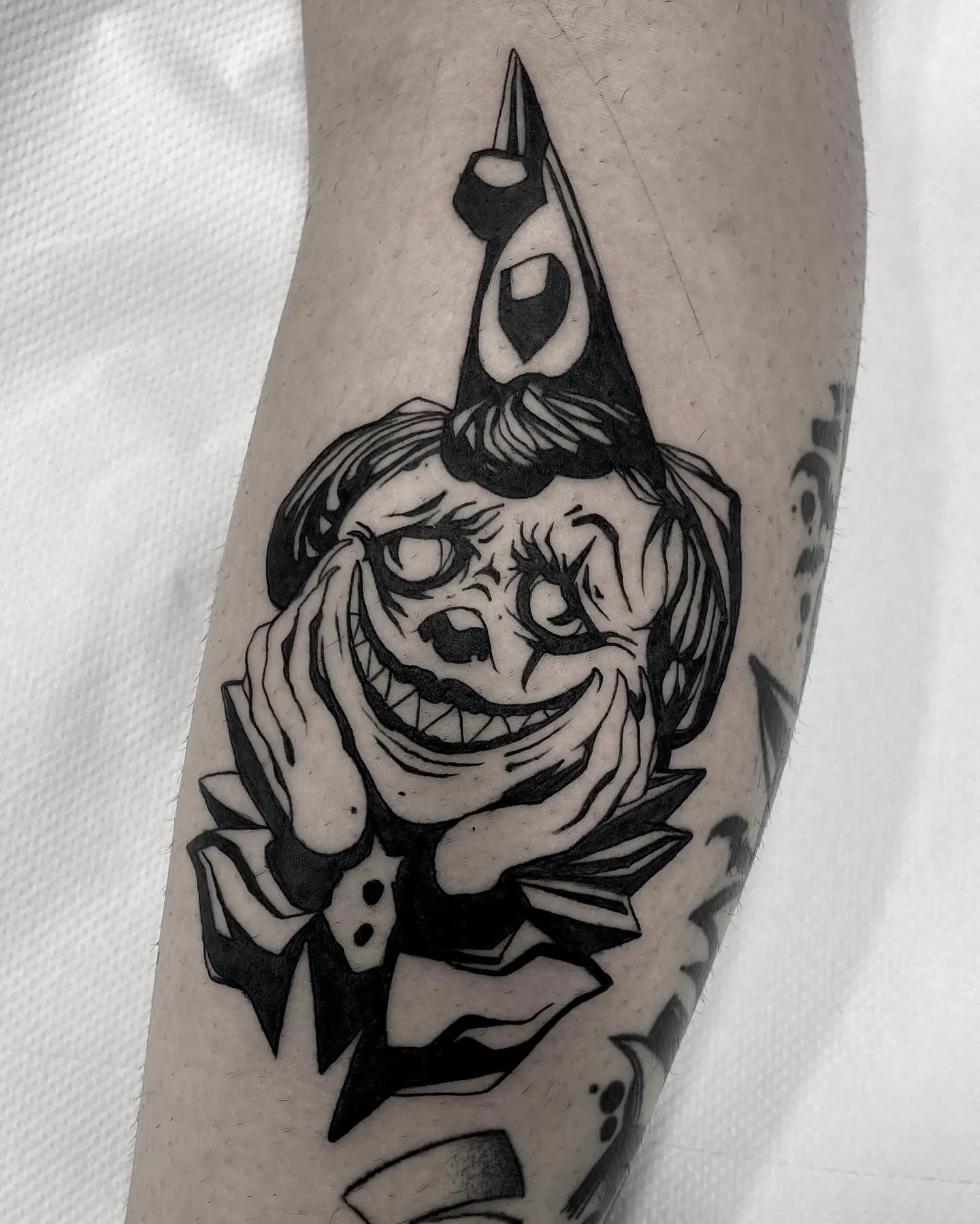 Tatuaje dark art de payaso con sonrisa perturbadora en el muslo