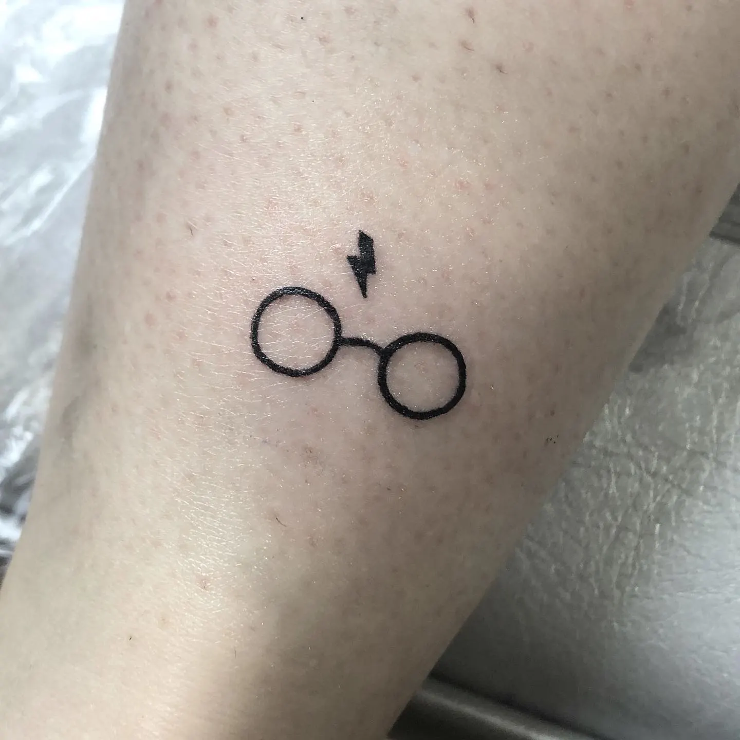 Tatuaje fine line de las gafas redondas de Harry Potter con la característica cicatriz en forma de rayo en la frente, en el antebrazo